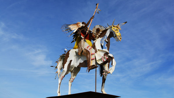 statue of white horse with native american warrior sitting on top of horse with a blue sky background
