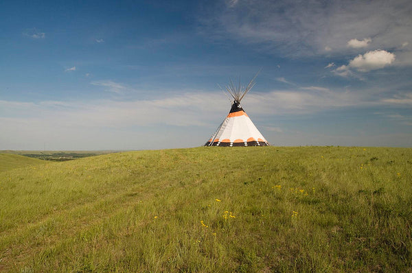 lone teepee on top of rolling grass with blue sky behind and some white clouds
